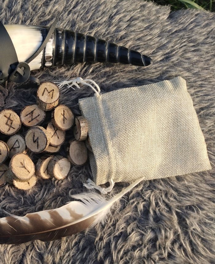Runas de madera junto a una bolsa de lino y un cuerno ritual